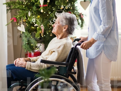Old woman in a wheelchair sitting by a Christmas tree